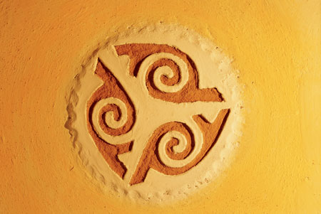 Earth plaster allows for fun moments such as this medallion. Kelly applied a thick layer of earth plaster, then let it set up slightly and pressed in the pattern with a shaped piece of 1/4-inch-thick Masonite. She used a hammer to create the scalloped edge, then colored the medallion with clay-based paints.
